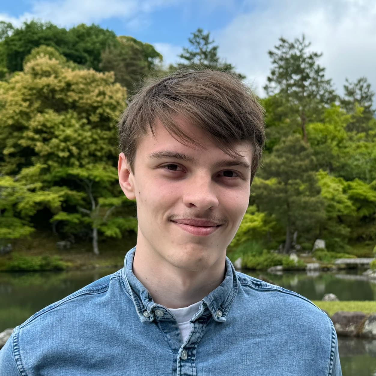 Maxime Bourand souriant dans un jardin entourant un lac